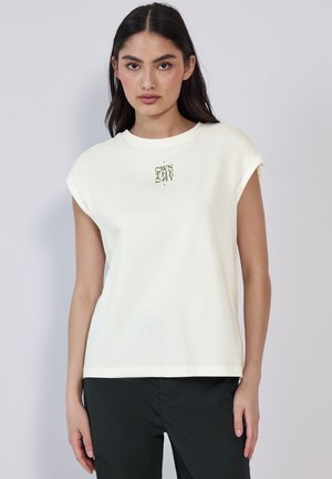 T-shirt en coton blanc avec des manches courtes roulées, arborant un graphique vert "PRENDRE LE CONTRÔLE DE LA JOURNÉE" sur le devant. Coupe droite à l'ourlet.