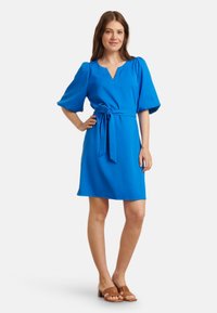 Heldere blauwe jurk met een V-halslijn, korte pofmouwen en een strik in de taille. Gladde stof met een ontspannen, A-lijn vorm. Eenvoudig ontwerp, minimale details.