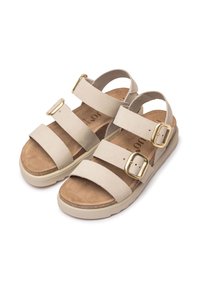 Beige suede sandals with three straps and gold buckles over a cork footbed, set on a light-colored rubber sole.