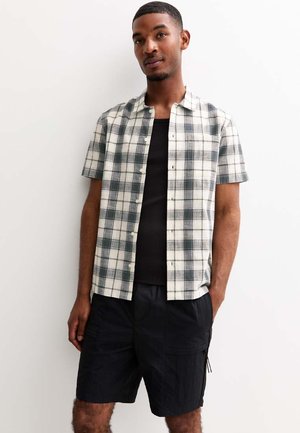 Chemise à manches courtes à carreaux blancs et verts, avec un col et un devant boutonné. Associée à un short cargo noir.