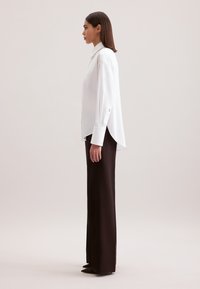 Camicia bianca a maniche lunghe con collo alto, abbinata a pantaloni scuri a vita alta, con vestibilità zip e tacchi a punta.