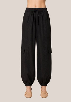 Pantaloni cargo neri a vita alta, ampi, con coulisse in vita, polsini elasticizzati, tasche con patta ai lati, indossati con ballerine beige con punta stretta.