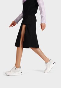 Sneaker bianche sportive con un motivo testurizzato, dettagli argentati e una suola ammortizzata, indossate con una gonna nera e un top a strati.