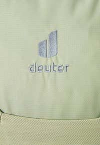 Világos zöld szövet, texturált felülettel, ezüst hímzett "deuter" logóval és geometrikus mintával a szöveg felett.