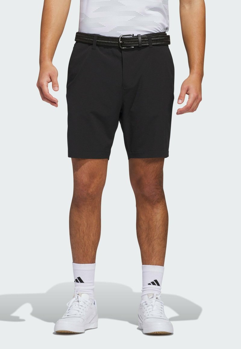Svarta shorts i ett smooth, lätt material, med framfickor och ett vävt svart bälte. Bärs med vita skor och strumpor.