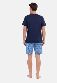 Navy short-sleeve T-shirt paired with blue patterned shorts featuring floral designs. Model is barefoot, viewed from the back.