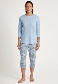 Lichtblauw langemouwen shirt met een borstzak, gecombineerd met een gepatternde cropped broek met een bloemenmotief in blauw en wit.