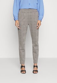 Uže pantalone s kariranim uzorkom u crnoj, bijeloj i bež boji s elegantnim dizajnom. Uparene s crnim sandalama s trakicama i plavom teksturiranom majicom.