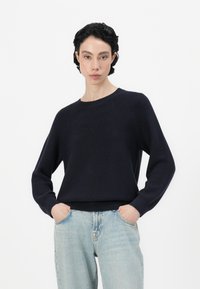 Ναυτικό μπλε πλεκτό πουλόβερ με μακριά ράγκλαν μανίκια και ριμπ τελείωμα. Συνδυασμένο με ανοιχτό μπλε τζιν παντελόνι. Χαλαρή εφαρμογή με λαιμόκοψη τύπου crew.