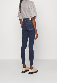 Högmidjade mörkblå denimjeans med smal passform, med två bakfickor och kontrasterande sömmar, bära med en randig topp och ljusa skor.