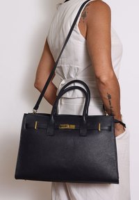 Zwart leren handtas met een gestructureerde afwerking, dubbele handgrepen, hardware in goudkleur en een afneembare schouderband.