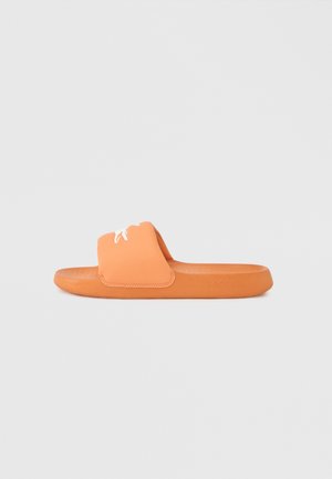 Sandalia tipo chancla naranja con una correa ancha, plantilla texturizada y suela moldeada. Presenta un logo blanco en la correa. Fabricada con material similar al caucho.