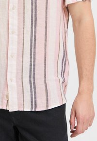 Camisa de botones de manga corta en rosa claro con rayas verticales en tonos más oscuros, que presenta un ajuste relajado y una tela texturizada.