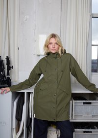 Alyvuogių žalios spalvos neperšlampama ilga striukė su aukštu apykakliu, reguliuojamomis raištelėmis, spaustukais ir dviem priekinėmis kišenėmis. Lygi tekstūra, laisvas, kasdienis modelis.