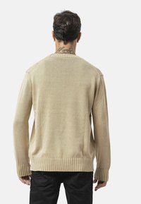 Beige gestrickter Pullover mit geripptem Saum und Ärmeln, der ein einfaches Design und strukturierte Stoffe aufweist, von hinten präsentiert.