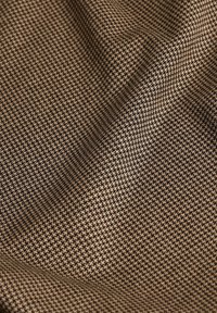Textiel met een houndstooth patroon in donkerbruin en beige, met een gestructureerde, geweven uitstraling en een zachte afwerking.