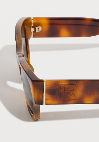 Κοντινό πλάνο σε καφέ γυαλιά ηλίου με μοτίβο χελώνας, βραχίονας με χαραγμένο λογότυπο "R" και λεπτομέρεια σε επίχρυσο μεντεσέ σε λευκό φόντο.