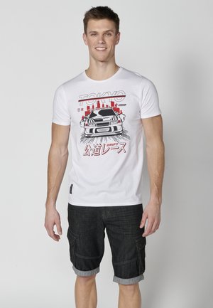 Tricou din bumbac alb cu un grafic al unei mașini și textul "Tokyo" în roșu. Asortat cu pantaloni scurți cargo din denim închisi la culoare, cu manșetele răsucite.