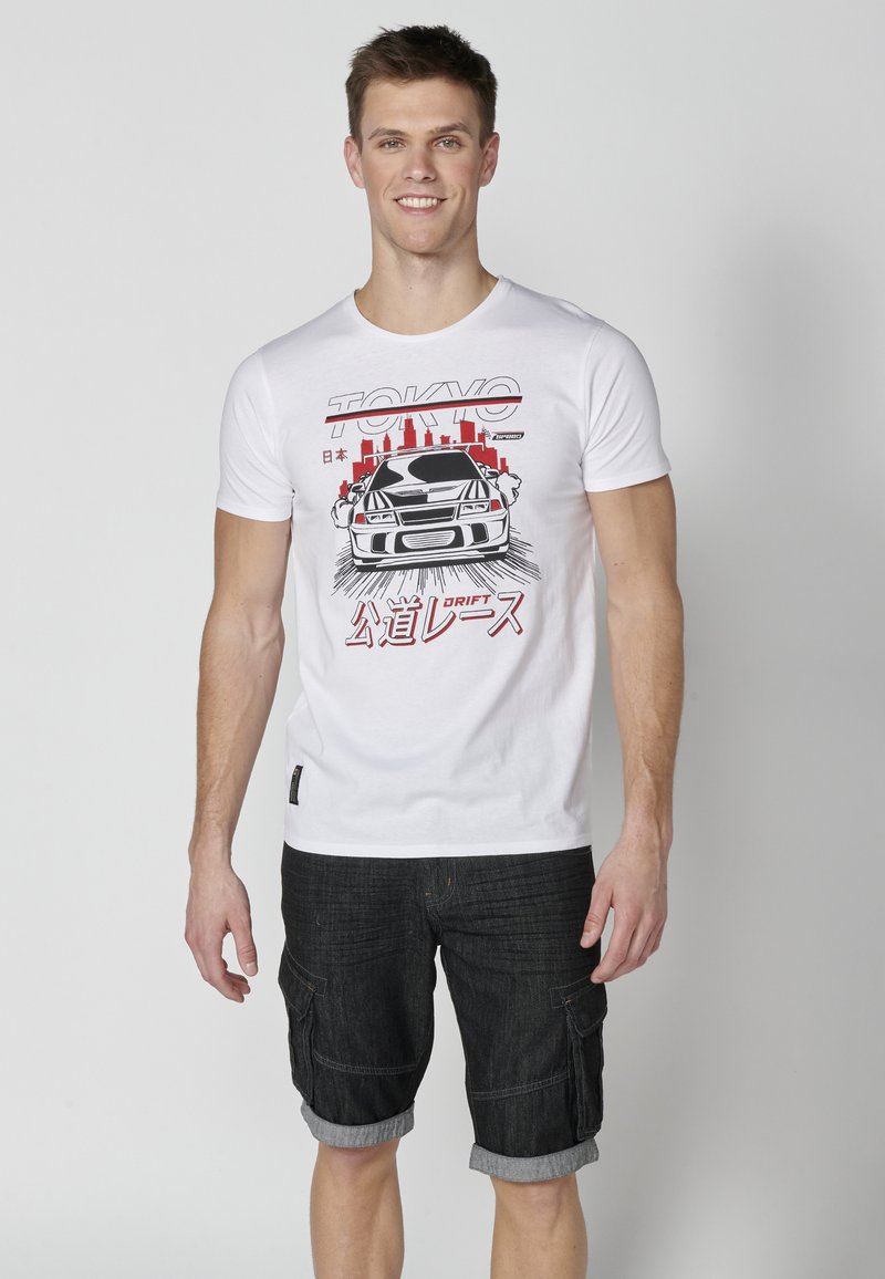 Tricou din bumbac alb cu un grafic al unei mașini și textul "Tokyo" în roșu. Asortat cu pantaloni scurți cargo din denim închisi la culoare, cu manșetele răsucite.