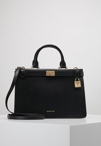 Borsa in pelle nera Michael Kors con manici superiori, dettaglio della chiusura dorata e tracolla staccabile su superficie bianca.