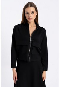 Czarna krótka kurtka zapinana na zamek z gładkiego materiału, posiadająca dwie kieszenie z przodu i wysoki kołnierz. Projekt zawiera srebrny zamek błyskawiczny i minimalne detale.