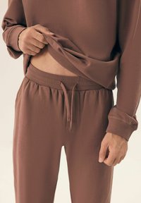 Brązowy zestaw odzieży do relaksu wykonany z gładkiego, elastycznego materiału. Bluza ma luźny krój, a spodnie posiadają elastyczny pas i sznurek do regulacji.