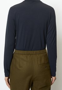 Navyblaues Langarmoberteil kombiniert mit olivgrünen Hose mit elastischem Bund, die eine Gesäßtasche und einen Knopfdetail aufweist. Glatte Stoffstruktur.