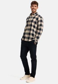 Das Flanellhemd für Herren hat ein kariertes Muster in Marineblau und Creme, lange Ärmel, einen geknöpften Kragen und eine weiche Textur. Es wird mit dunklen Hosen und hellen Schuhen kombiniert.