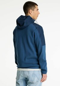 Sötétkék kapucnis fleece dzseki, sima textúrával, kontrasztos tengerészkék vállpanelekkel és laza fazonnal. További részletezések közé tartozik egy kenguruzseb.