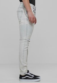 Világoskék, szakadt térdnál skinny farmernadrág, fémből készült lánc részletekkel és kontrasztos varrással, fekete, alacsony szárú sportcipővel párosítva.
