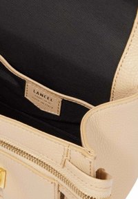Sac à main en cuir beige avec une surface texturée, doté d'une doublure noire, de quincaillerie dorée, et d'une étiquette portant la mention "LANCEL, Fabriqué en Italie."