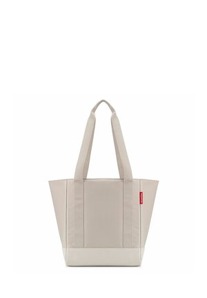 Sac cabas beige avec de larges poignées et une petite étiquette rouge sur le côté, présenté sur un fond blanc uni.