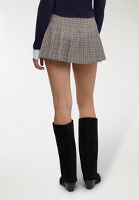 Gonna corta plissettata in tessuto a quadri, con motivi blu, gialli e bianchi. Stivali neri al ginocchio in suede con tacco spesso.