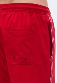 Κόκκινα αθλητικά σορτς με ελαστική μέση, πλαϊνές τσέπες και μία πίσω τσέπη με οπές. Διαθέτουν λογότυπο Calvin Klein κατά μήκος της πλευράς.