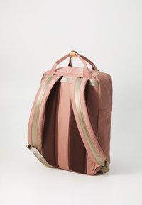 Sac à dos en tissu rose avec des accents dorés. Inclut un dos rembourré, deux poignées supérieures, des bretelles réglables et une poche latérale. Panneaux texturés visibles.