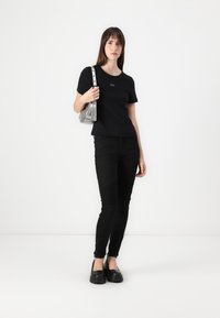 T-shirt noir GAP avec un col rond, associé à un jean skinny noir avec des accents côtelés et des zips aux chevilles, porté avec des chaussures à plateforme noires.