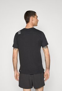 Sort kortærmet t-shirt med runde halsudskæring, struktureret stof og et logo på den øverste ryg. Parret med mørke shorts, er stilen afslappet.