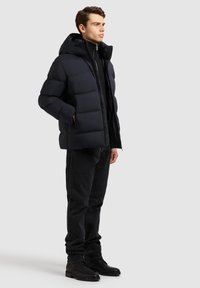 Tengerészkék pufikabát levehető kapucnival, steppelt mintával, elülső cipzárral és oldalsó zsebekkel, fekete farmernadrággal és csizmával párosítva.