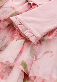 Abito in tulle rosa con motivo floreale, balze sovrapposte e una manica in cotone morbido e testurizzato con un dettaglio di orlo arricciato.