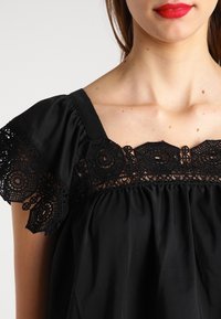 Blusa nera con bordo in pizzo, caratterizzata da maniche corte a volant e scollo quadrato. Tessuto morbido con dettagli arricciati attorno al busto.