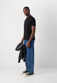 Schwarzes Poloshirt mit kurzen Ärmeln, blaue weite Jeans, schwarze Lederjacke in der Hand und schwarze Leinenschuhe mit weißen Sohlen. Einfaches Design.
