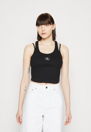 Débardeur noir court avec une texture côtelée et des bretelles spaghetti ajustables. Présente un patch logo CK rectangulaire à l'avant.