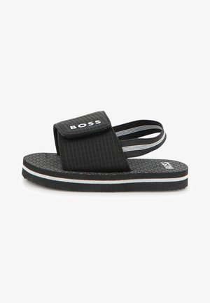 Mustast tekstiilist ülemise osaga slaid-sandaal, reguleeritava rihma ja polsterdatud tallaga. Kaunistatud valgete ja helesiniste horisontaalsete triipudega.