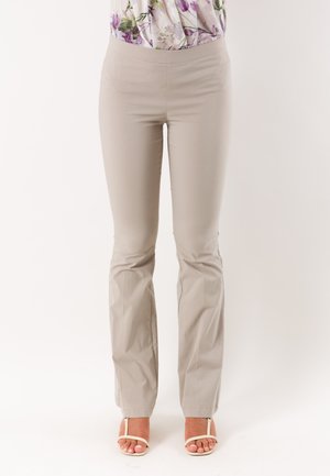 Primo piano di una persona che indossa pantaloni beige a gamba dritta e sandali bianchi con tacco e punta aperta, con un top floreale infilato dentro.