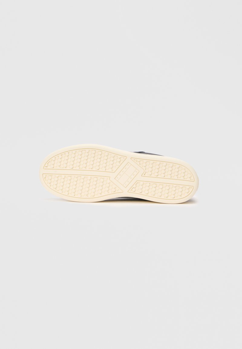 Black athletic shoe with a textured rubber sole; cream-colored outsole with a dotted pattern and distinctive design for traction.