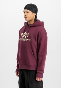 Sudadera burdeos hecha de una mezcla de algodón, con un bolsillo delantero y capucha con cordón. El logo de la marca está impreso en crema en el pecho.