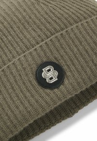Berretto lavorato a maglia verde oliva con texture a coste; presenta una toppa in pelle nera con dettagli logo argentati.