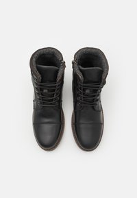 Botas de cuero negras con puntera redonda, con cordones en la parte delantera, cremalleras laterales y forro texturizado gris. Suela de goma con detalles en marrón.