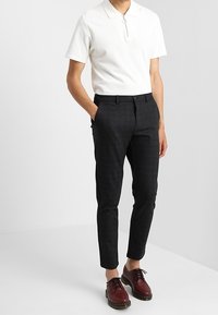 Witte polo met korte mouwen en ritskraag, gecombineerd met donkere, gemêleerde slim-fit broek en bordeauxgekleurde veterschoenen.