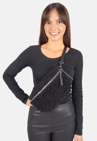 Schwarze Tasche aus strukturiertem Fell mit diagonaler Form, silbernem Reißverschluss und Lederriemen. Die Tasche verfügt über zwei Lederakzente.